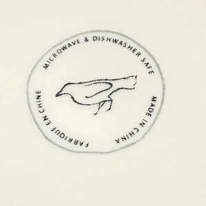 May include: A circular emblem with a bird illustration and text. The text reads "MICROWAVE & DISHWASHER SAFE", "FABRIQUE EN CHINE", and "MADE IN CHINA". The bird is a simple, sketched design.