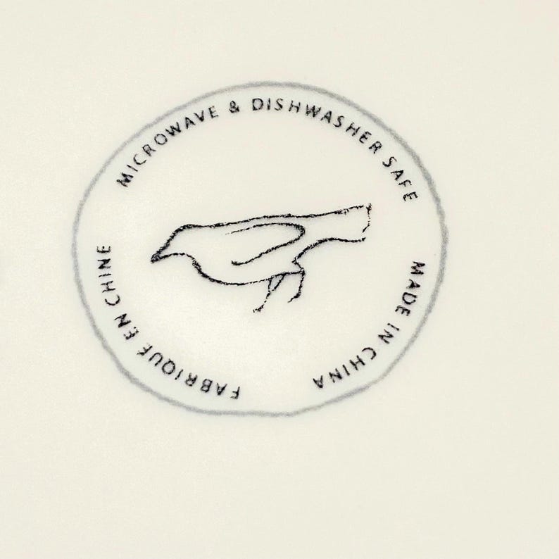 May include: A circular emblem with a bird illustration and text. The text reads "MICROWAVE & DISHWASHER SAFE", "FABRIQUE EN CHINE", and "MADE IN CHINA". The bird is a simple, sketched design.