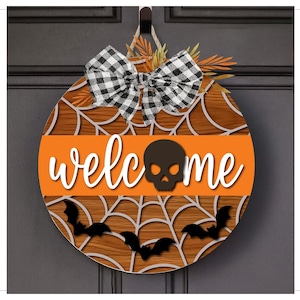 Puede incluir: Cartel de bienvenida redondo de madera de Halloween con un diseño de telaraña y la palabra "welcome". El cartel presenta una calavera negra, murciélagos y un lazo a cuadros blanco y negro. El fondo es un patrón de vetas de madera.
