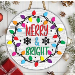 May include: Round wooden sign with the words "MERRY & BRIGHT" in red and green, surrounded by a string of colorful Christmas lights. The sign has a rope for hanging and is decorated with snowflakes.