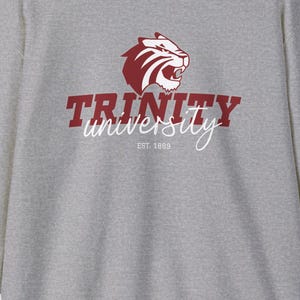 May include: A heather gray crew neck sweatshirt with the Trinity University logo. The logo features a maroon tiger head above the word "TRINITY" and the word "university" in a script font. The text "EST. 1869" is below the word "university".
