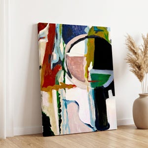 May include: Abstract art canvas print featuring a bold composition of shapes and colors. The artwork includes a large black circle, a pink half-circle, and vertical strokes of red, blue, and green. The canvas is leaning against a white wall on a wooden floor.