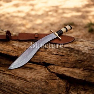 Puede incluir: Un cuchillo grande, de color plateado, con una hoja curva, apoyado sobre una superficie de madera. El cuchillo tiene un mango de color claro con detalles negros y una guarda de latón. Se ve una funda de cuero marrón. La palabra "Sitecture" está impresa en la hoja.
