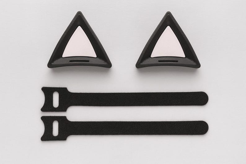 Puede incluir: Un conjunto de accesorios negros con forma de orejas de gato y un interior blanco, junto con dos bridas de velcro negras. Los art&iacute;culos est&aacute;n dispuestos sobre un fondo blanco, adecuados para cosplay o disfraces.