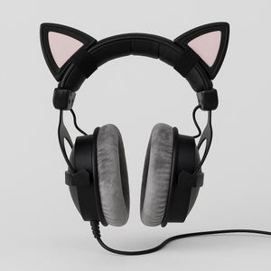 Puede incluir: Auriculares negros con almohadillas grises y orejas de gato. Las orejas de gato son negras con el interior rosa. Los auriculares tienen un cable negro y est&aacute;n sobre un fondo blanco.