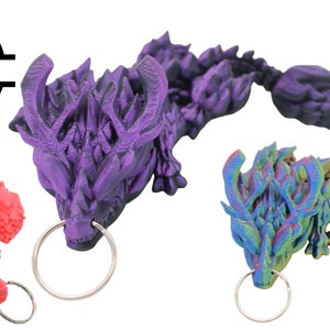 Puede incluir: Tres llaveros de dragón impresos en 3D en diferentes colores: rosa, morado e iridiscente. Cada llavero presenta un diseño de dragón detallado con un anillo de llave plateado.