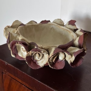 May include: A small ceramic bowl with a white glaze and brown accents. The bowl is shaped like a flower with petals around the rim.
