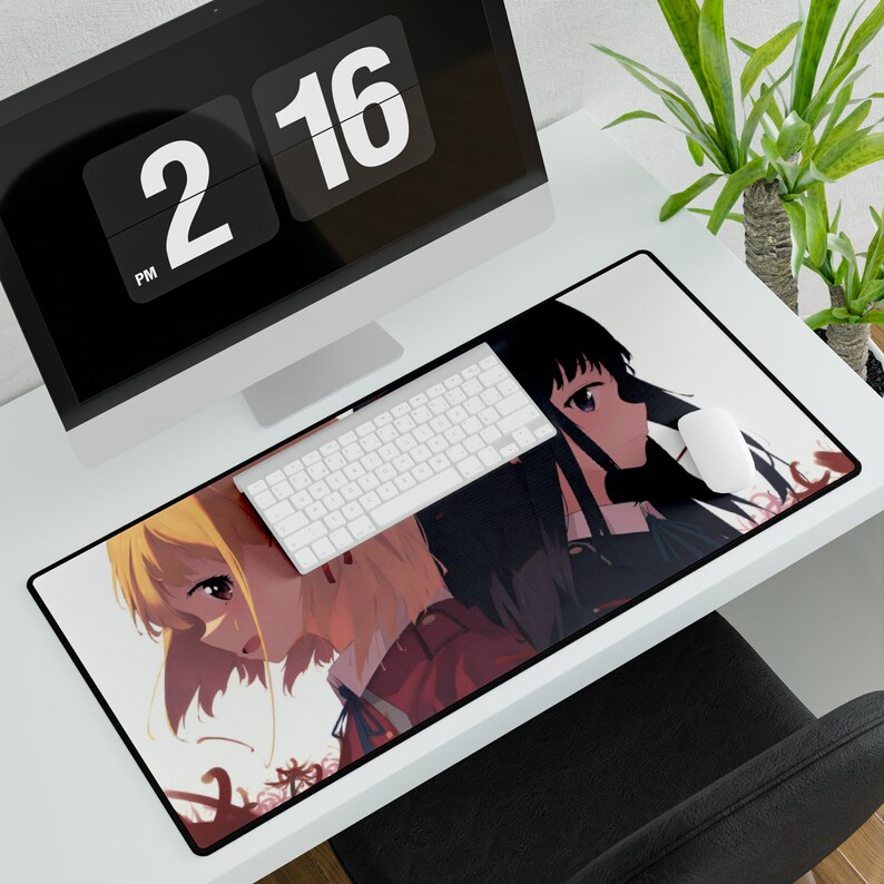 May include: A white desk mat with a black border features an anime illustration of two girls with long hair. One girl has long black hair and the other has long blonde hair. The girls are looking at each other. The background is a light pink color with a floral pattern.