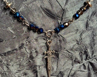 May include: A silver chain necklace with dark blue glass beads and a silver sword pendant.