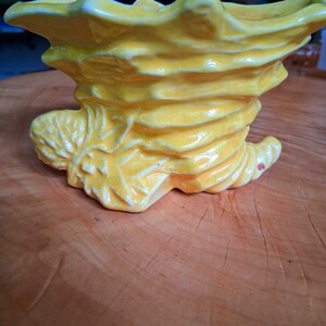 May include: A bright yellow ceramic cornucopia planter featuring a textured, leaf-like exterior with a glossy finish and visible fine crackle patterns throughout the glaze. The vessel has a wide, flared opening and a tapered, curved base.