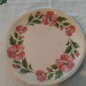 May include: A white oval ceramic serving platter with a floral design. The design features pink poppies with green leaves and stems around the edge of the platter.
