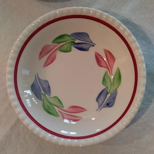 May include: A white ceramic bowl with a red rim and a decorative design of green, blue, and pink leaves around the center.