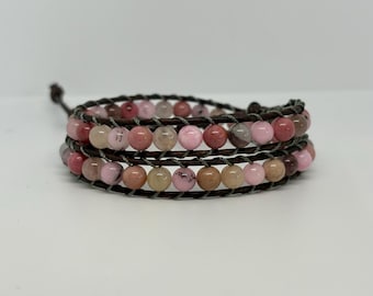 May include: Wrap bracelet featuring multiple strands of brown leather and colorful, round beads in shades of pink, brown, and tan. The bracelet is wrapped around itself and secured with a leather tie.