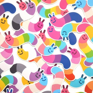 May include: A collection of colorful worm-shaped stickers with different pride flag designs. The stickers feature a smiling face and two antennae.