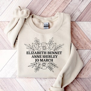 May include: A beige sweatshirt with a black floral design and the text "Elizabeth Bennet Anne Shirley Jo March" printed on the front.