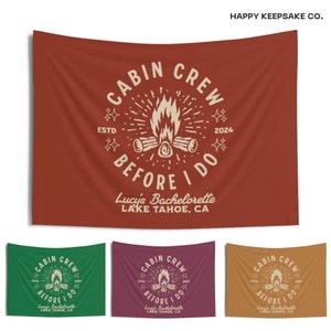 May include: A red, green, purple, and orange fabric banner with the text "Cabin Crew Before I Do" and a campfire graphic. The banner also includes the text "Lucy's Bachelorette Lake Tahoe, CA" and the dates "ESTD 2004".
