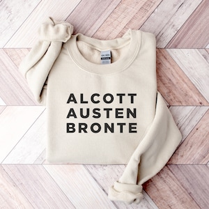 May include: A beige sweatshirt with the text "ALCOTT AUSTEN BRONTE" printed in black.