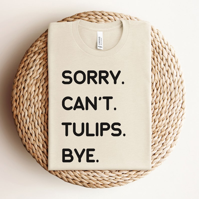 K&ouml;nnte beinhalten: Ein beiges T-Shirt mit schwarzem Text, der "SORRY. CAN'T. TULIPS. BYE." lautet.
