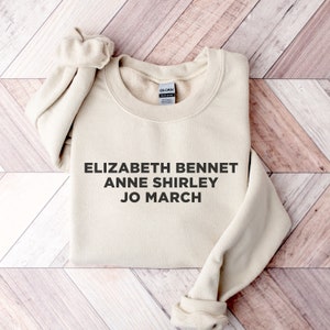May include: A beige sweatshirt with the text "Elizabeth Bennet Anne Shirley Jo March" printed on the front.
