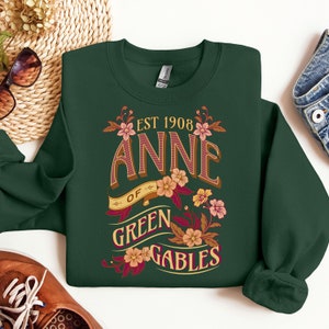 May include: A dark green sweatshirt with a floral design and the text "EST 1908 ANNE OF GREEN GABLES".
