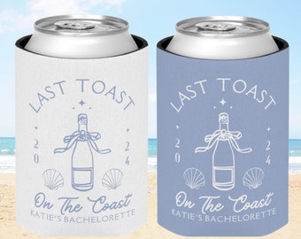 May include: Two white and blue can coolers with the text "Last Toast On The Coast Katie's Bachelorette" and a champagne bottle with a ribbon and seashells.