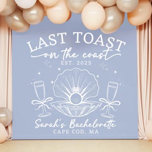 May include: A light blue backdrop with white text that reads "Last Toast on the Coast Est. 2025" and "Sarah's Bachelorette Cape Cod, MA". A white illustration of a seashell with a pearl and a diamond inside, and two champagne glasses on either side.