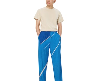 May include: A person wearing a light beige t-shirt and blue pants with a white abstract design. The pants have an elastic waistband and pockets.