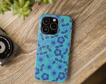 May include: A teal phone case with a floral pattern of blue flowers and leaves. The case is on a wooden surface, with a camera and plant in the background. The case has a glossy finish and a protective design.