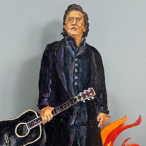 May include: A painting of a man in a black suit holding a black acoustic guitar. He is standing in front of a background of orange flames.