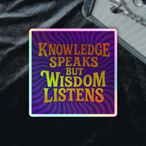 Op de afbeelding: Vierkante sticker met de tekst "KNOWLEDGE SPEAKS BUT WISDOM LISTENS" in oranje en geel tegen een paarse en blauwe golvende achtergrond. De sticker heeft een holografische rand.