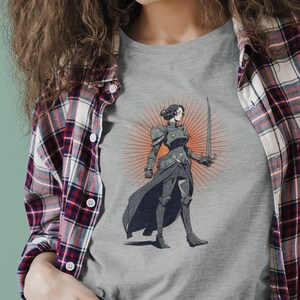 May include: A gray t-shirt with a graphic of a woman in armor holding a sword. The woman is standing in front of a sunburst.