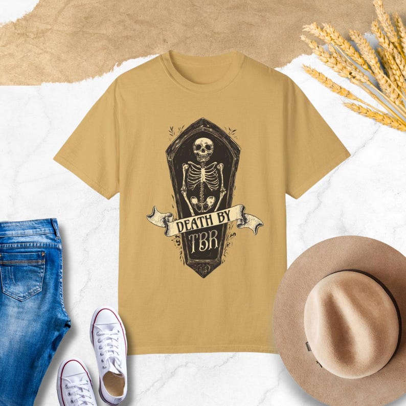 May include: A mustard yellow t-shirt with a graphic of a skeleton in a coffin. The text "Death by TBR" is printed on the coffin.