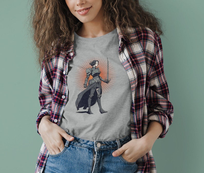 May include: A gray t-shirt with a graphic of a woman in armor holding a sword. The woman is standing in front of a sunburst.