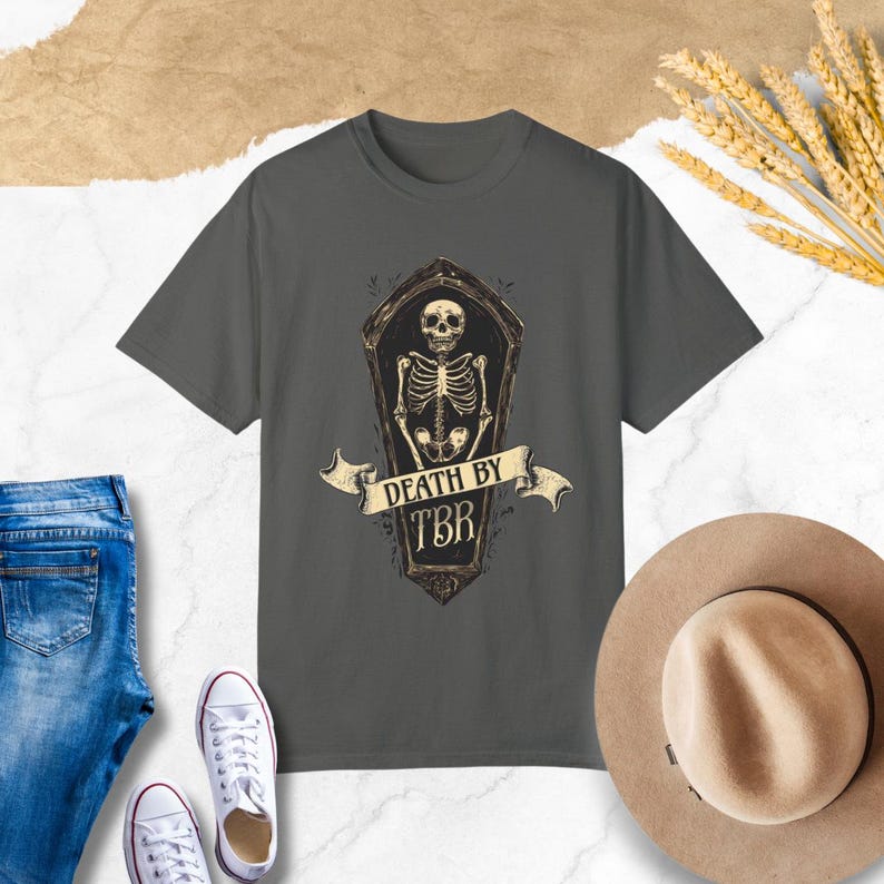 May include: A dark gray t-shirt with a graphic of a skeleton in a coffin. The text "Death by TBR" is printed on the shirt.