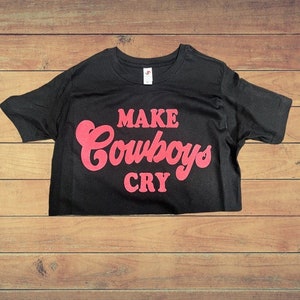 Puede incluir: Camiseta negra con el texto "MAKE COWBOYS CRY" en letras rosas.