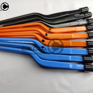 Peut inclure: Une collection de pinces chirurgicales au design ergonomique coudé avec des manches noirs, orange et bleus. Chaque instrument possède une pointe cylindrique noire et un petit trou circulaire près du coude. Le logo Celta International est visible.