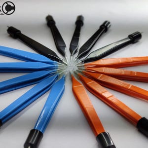 May include: A collection of surgical bipolar forceps arranged in a circular pattern, featuring black, blue, and orange handles with black end caps. The Celta International logo is visible in the top left corner of the image.
