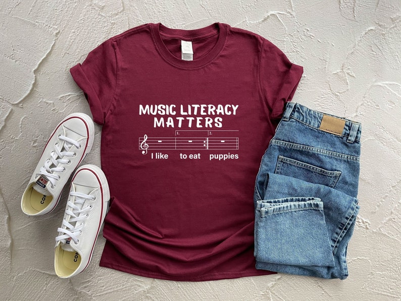 May include: Burgundy t-shirt with white text that reads "Music Literacy Matters" and a musical staff with the words "I like to eat puppies".
