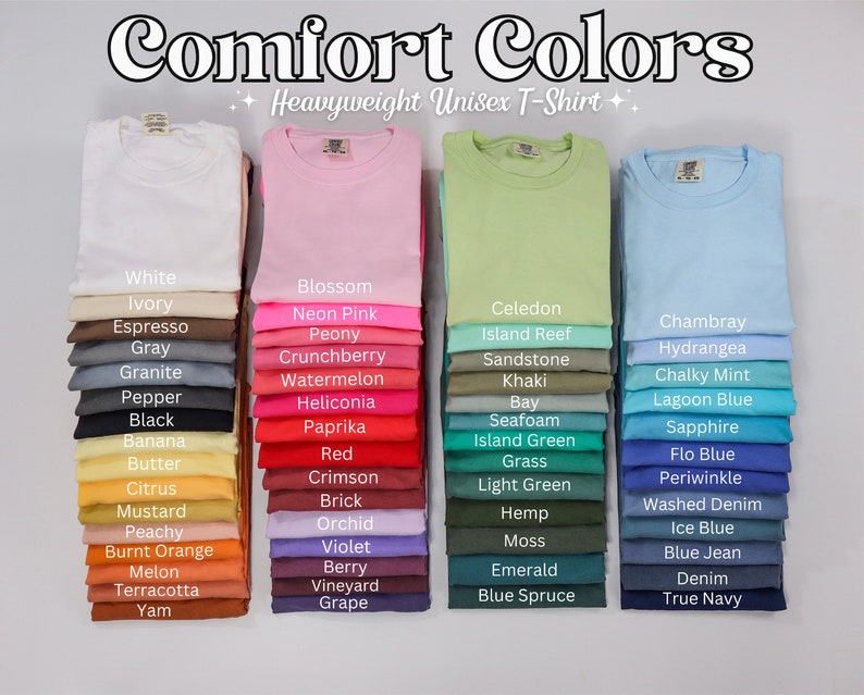 Op de afbeelding: Afbeelding met een verscheidenheid aan Comfort Colors unisex t-shirts van zwaar gewicht in een spectrum van kleuren. De afbeelding toont stapels opgevouwen shirts, elk in een andere tint, met kleurnamen zoals "White", "Blossom" en "Chambray" eronder. De tekst "Comfort Colors" staat bovenaan.