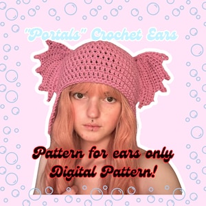 May include: A pink crochet hat with large, pointed ears. The hat is worn by a person with pink hair and a nose ring. The text "Portals" Crochet Ears" is at the top of the image. The text "Pattern for ears only Digital Pattern!" is at the bottom of the image.