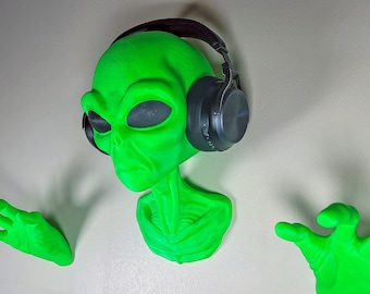 May include: A green alien bust with headphones on, wearing a serious expression. The alien has two outstretched hands, one on each side of the bust.