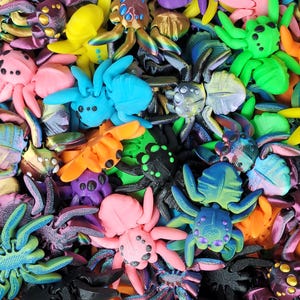 Puede incluir: Primer plano de una colección de arañas de juguete en una variedad de colores brillantes, incluyendo azul, verde, naranja, rosa, amarillo y negro. Las arañas son detalladas y están dispuestas en un patrón denso y superpuesto, creando una exhibición vibrante y juguetona.
