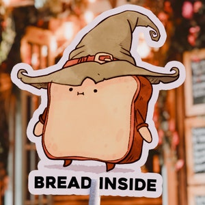 May include: A cartoon illustration of a slice of bread wearing a brown wizard hat with a gold buckle. The bread has a smiling face and the text "BREAD INSIDE" is written below it.