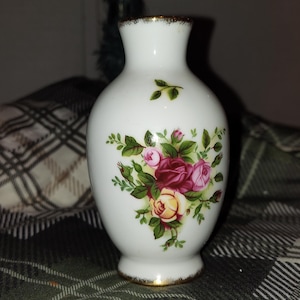 以下が含まれることがあります： 金色の縁と底が付いた、小さな白いセラミック花瓶。 ピンク、赤、黄色のバラと緑の葉のフローラルデザインで装飾されています。 花瓶は細い首と丸みを帯びたボディをしています。