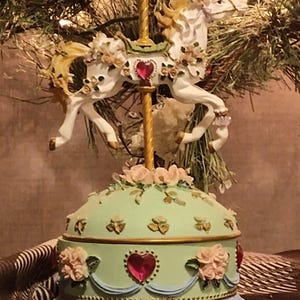 Może przedstawiać: Biały ceramiczny kubek z czarnym uchwytem i napisem "But First, Coffee" pogrubioną, czarną czcionką. Kubek jest umieszczony na rozmytym tle, sugerującym przytulne otoczenie.