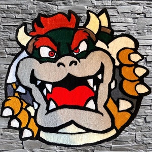 Op de afbeelding: Een pluche vloerkleed met een cartoonfiguur met een rode mohawk, een groene schildpadschelp en een grote, tandenrijke grijns. Het personage wordt afgebeeld met een woeste uitdrukking en houdt een grote, geklauwde hand vast.