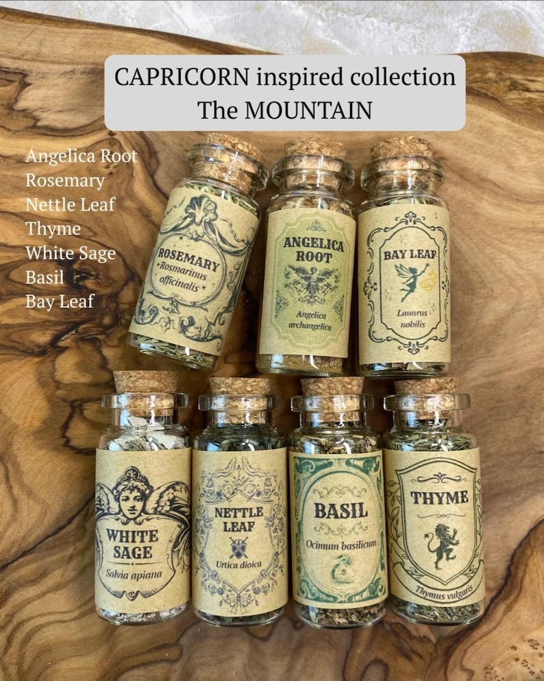 May include: Seven clear glass apothecary jars with cork stoppers, each containing dried herbs labeled Rosemary, Angelica Root, Bay Leaf, White Sage, Nettle Leaf, Basil, and Thyme. The text reads CAPRICORN inspired collection The MOUNTAIN.