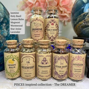 May include: Seven small glass jars with cork stoppers, each containing dried herbs labeled Jasmine, Holy Basil, Lemon Balm, Mugwort, Wormwood, Star Anise, and Lavender. The labels feature decorative borders and botanical names in a tan paper finish.