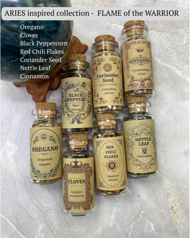 May include: A collection of seven clear glass spice jars with cork stoppers, each featuring a tan label with decorative borders and text including ARIES inspired collection - FLAME of the WARRIOR, Oregano, Cloves, Black Pepper, Coriander Seed, Red Chili Flakes, Nettle Leaf, and Cinnamon.