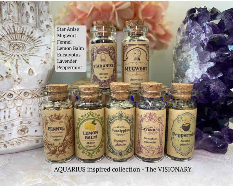 May include: A collection of seven small glass jars with cork stoppers, each containing dried herbs labeled Star Anise, Mugwort, Fennel, Lemon Balm, Eucalyptus, Lavender, and Peppermint. The labels feature ornate, vintage-style typography and decorative borders.